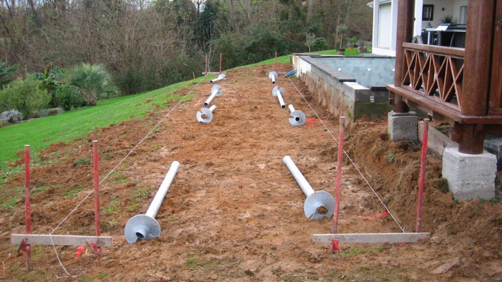 Ground preparation for raised decking with steel screw piles installed beside a garden property