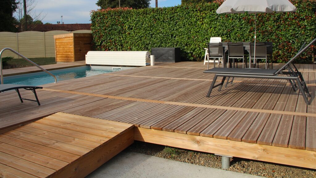Timber poolside decking area with sun loungers, outdoor dining furniture and garden screening